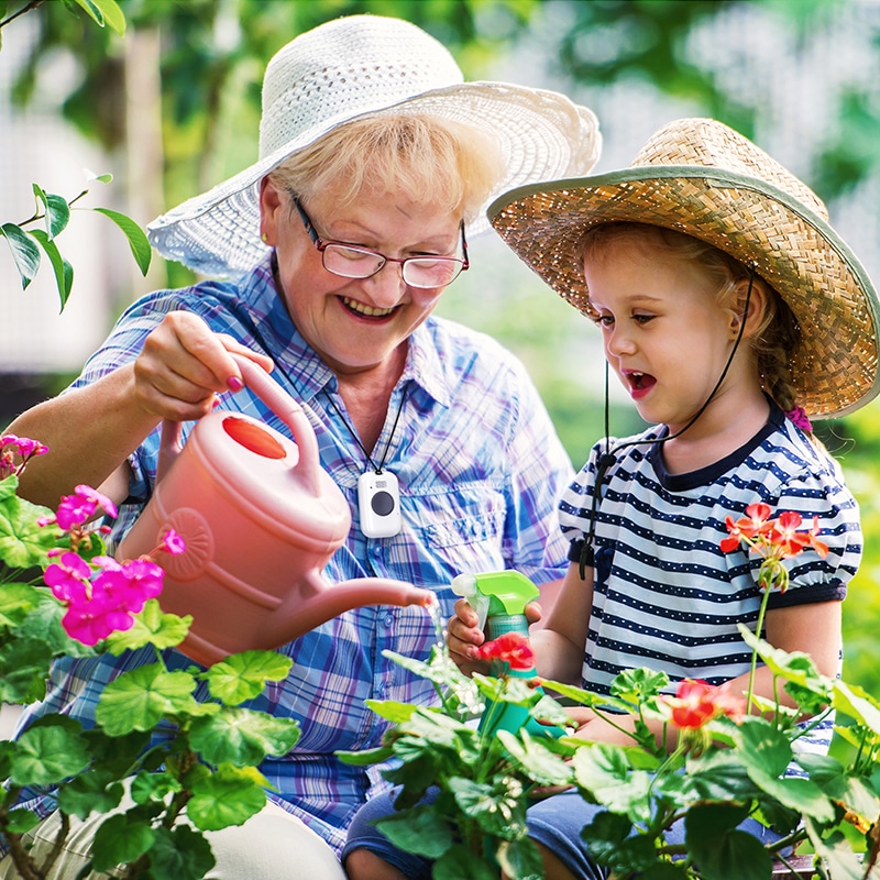 Grandmother wearing On the Go medical alert system in the garden with granddaughter
