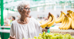 Potassium rich foods for seniors including bananas selected by an older woman at a grocery store