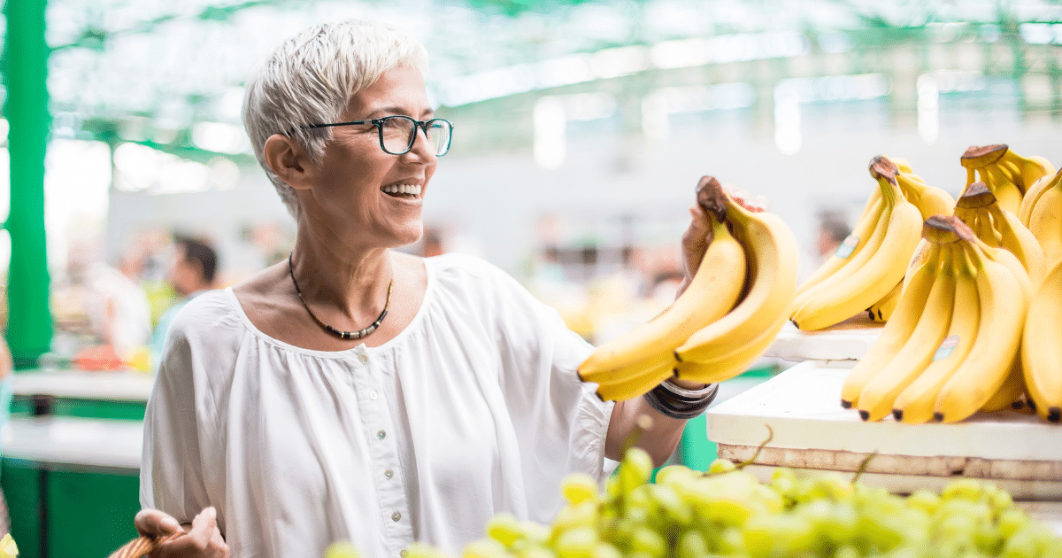 Potassium rich foods for seniors including bananas selected by an older woman at a grocery store