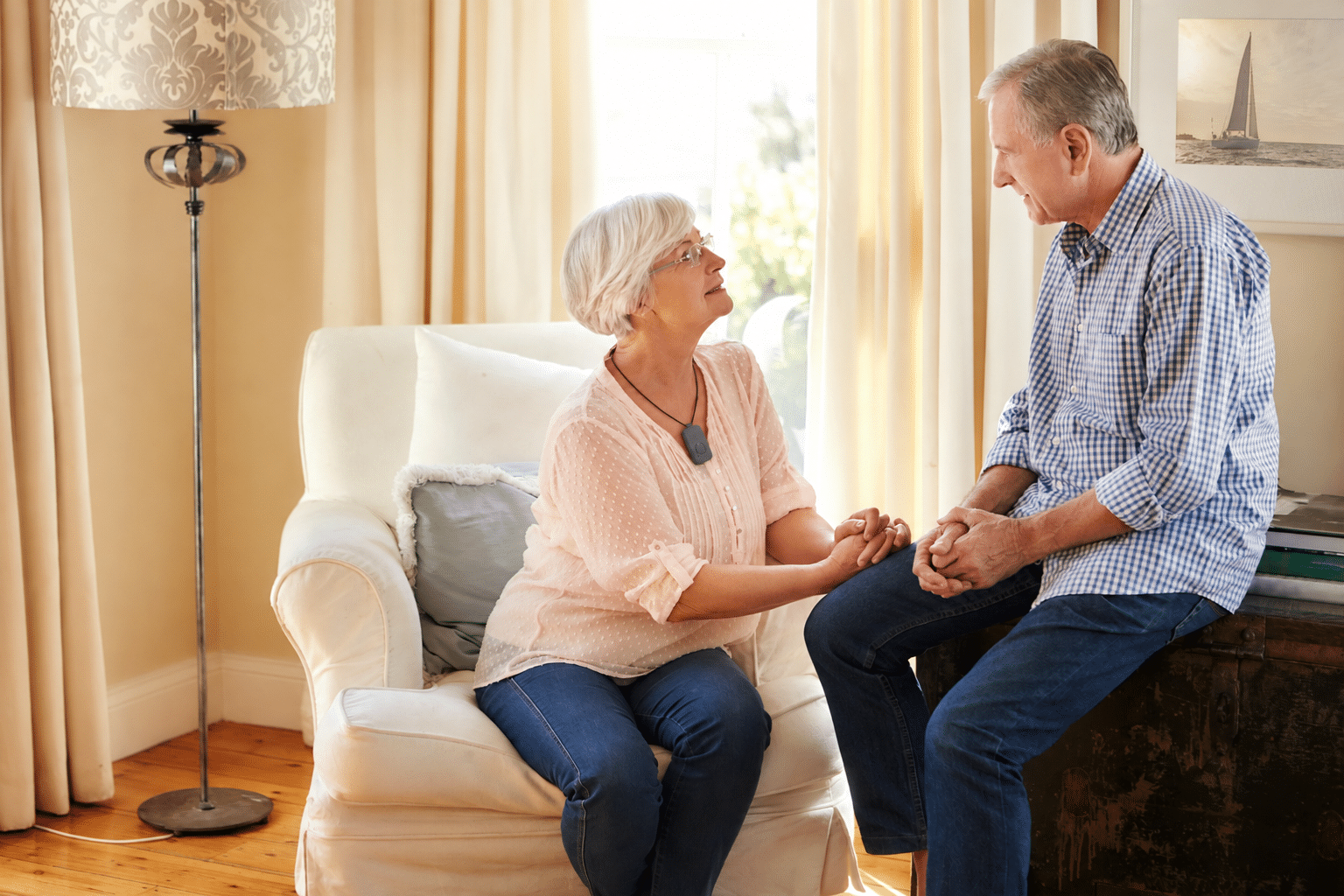 Senior woman wearing a medical alert pendant while talking with her husband at home, highlighting monitoring devices for seniors.