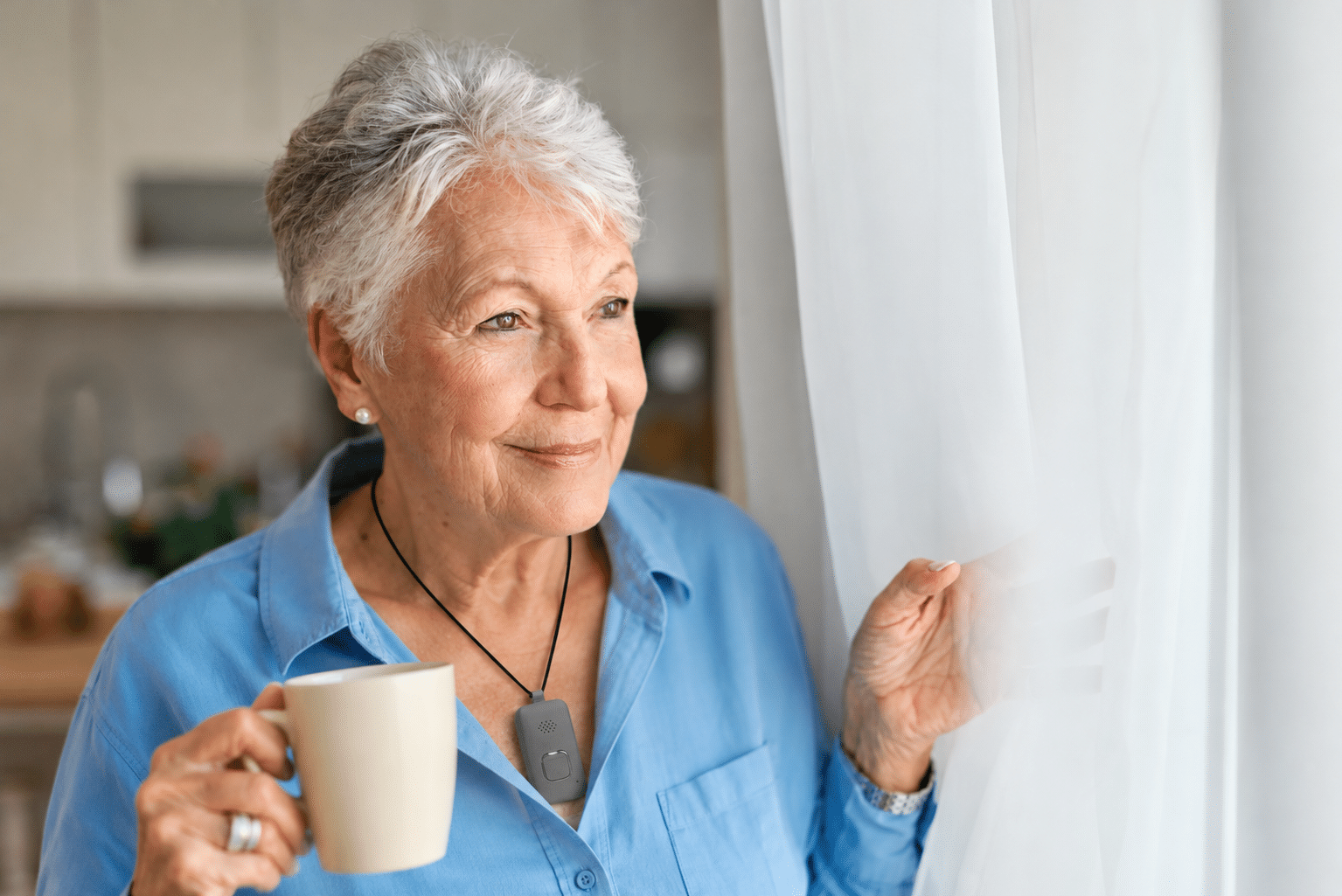 Senior woman wearing a personal emergency response system pendant while enjoying her morning coffee by the window.